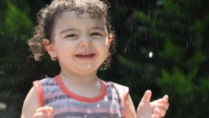 A young girl smiles as she plays in a sprinkler